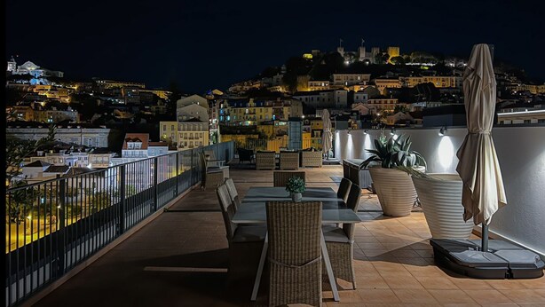 Une terrasse sur le toit avec des sièges extérieurs, une vue sur le paysage urbain la nuit et une grande plante en pot.