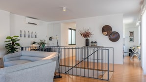 Un salon moderne avec un canapé gris, un coin repas comprenant une table et des chaises, et un escalier menant à un autre niveau.