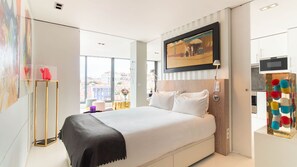 A modern hotel room with a large bed, a TV mounted on the wall, and a view of the city through large windows. - Full Sky in Chiado by LovelyStay (Encarnação)
