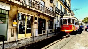 A tram on a track, a building with a sign reading 'SOUSA,' and a street with parked cars. - Full Sky in Chiado by LovelyStay (Encarnação)
