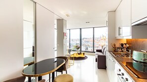 A modern kitchen with a view of the city, a dining area with a glass table, and a sofa. - Full Sky in Chiado by LovelyStay (Encarnação)