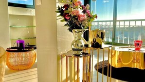 A room with a large window, a decorative vase with flowers, a small table with a glass top, and a wicker basket. - Full Sky in Chiado by LovelyStay (Encarnação)
