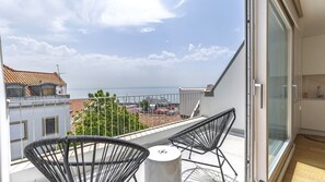 A balcony with two black wicker chairs, a small table, and a glass door leading to a kitchen area. - Penthouse on the Tagus in Alfama by LovelyStay (Lisboa)