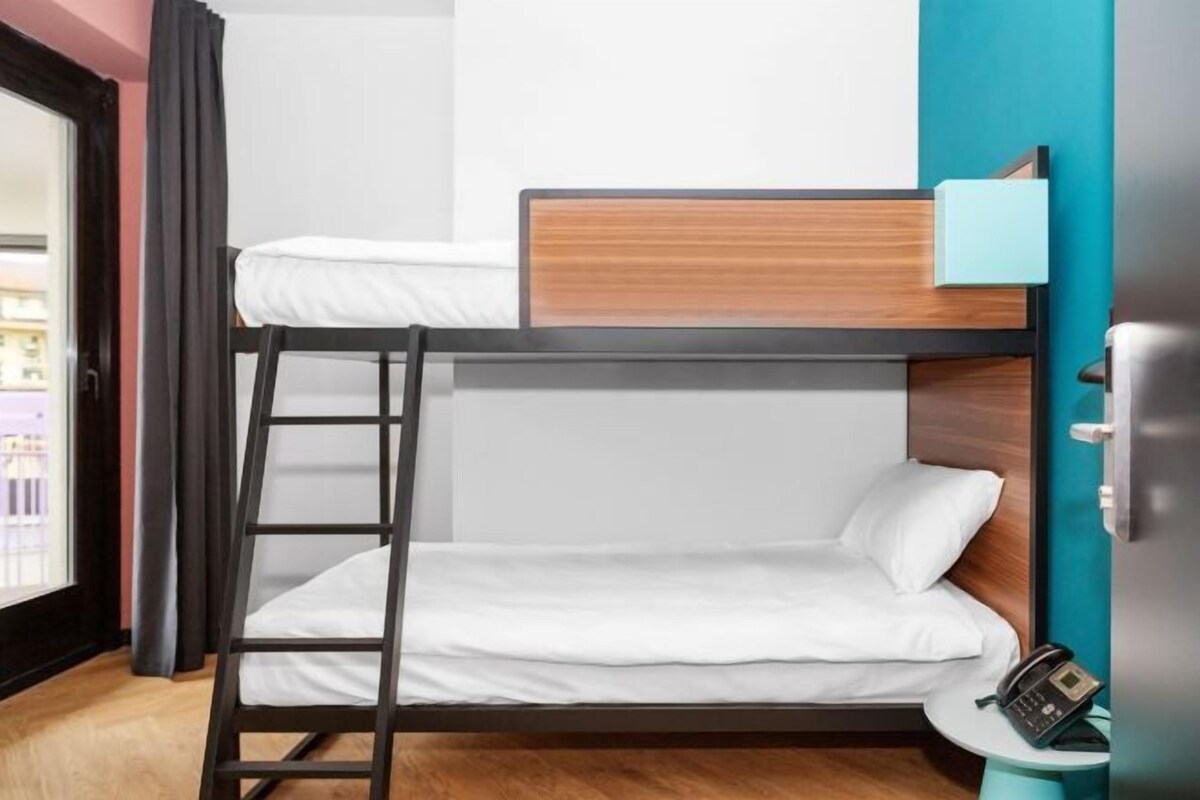 A bunk bed with a ladder, a bedside table with a phone, and a view of the outside.