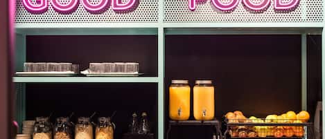 A food display with jars of grains, a juice dispenser, and a tray of oranges.