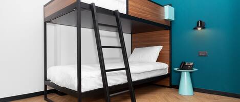 A bunk bed with a ladder, white bedding, a teal accent wall, a small side table with a phone, and a wooden floor.