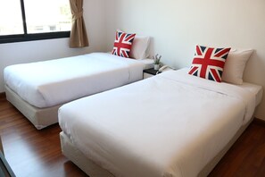 Two single beds with white bedding and British flag pillows, a nightstand with a phone and a small plant, and a window with curtains. - OYO 338 V-twin Donjan Service Apartment (Chiang Mai)