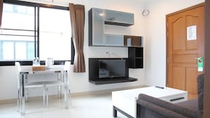 A modern, well-lit room with a dining table, chairs, a sofa, a flat-screen TV, and a wooden door.