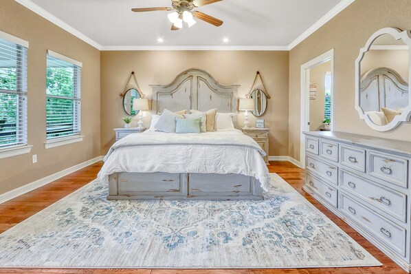 A bedroom with a large bed, a dresser, two nightstands, a ceiling fan, and a large mirror.