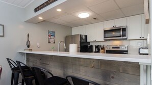 Une cuisine avec des armoires blanches, un plan de travail en bois et un coin bar avec des chaises noires.