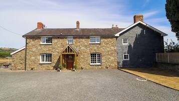 A two-story stone house with a wooden front door, multiple windows, and a chimney.