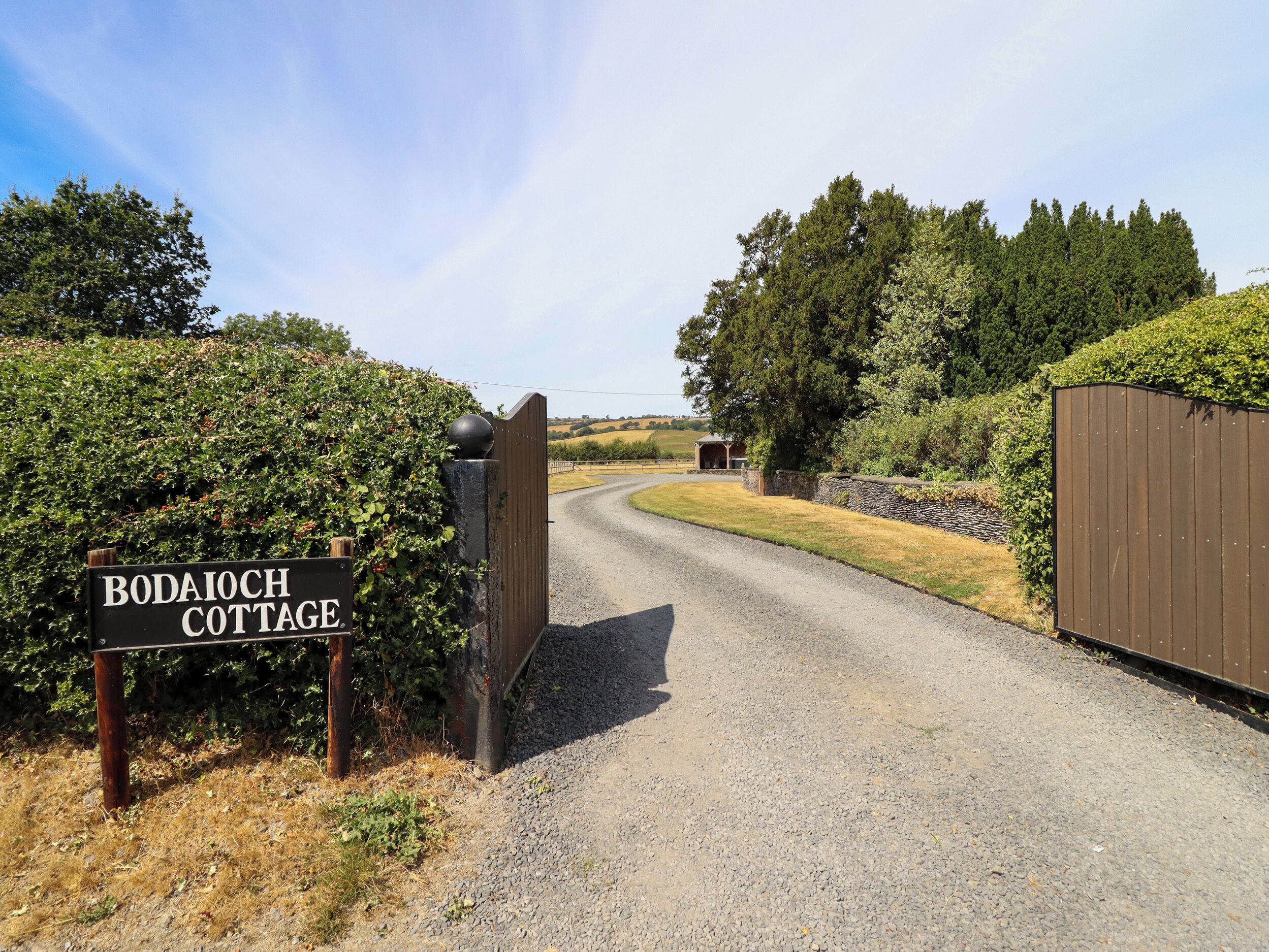 A gravel driveway leading to a gated entrance with a sign reading 'Bodaioch Cottage.'
