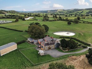 A rural property with a large barn, a circular pond, and expansive green fields. - Bodaioch Cottage (Caersws)