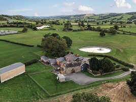 A rural property with a large barn, a circular pond, and expansive green fields.