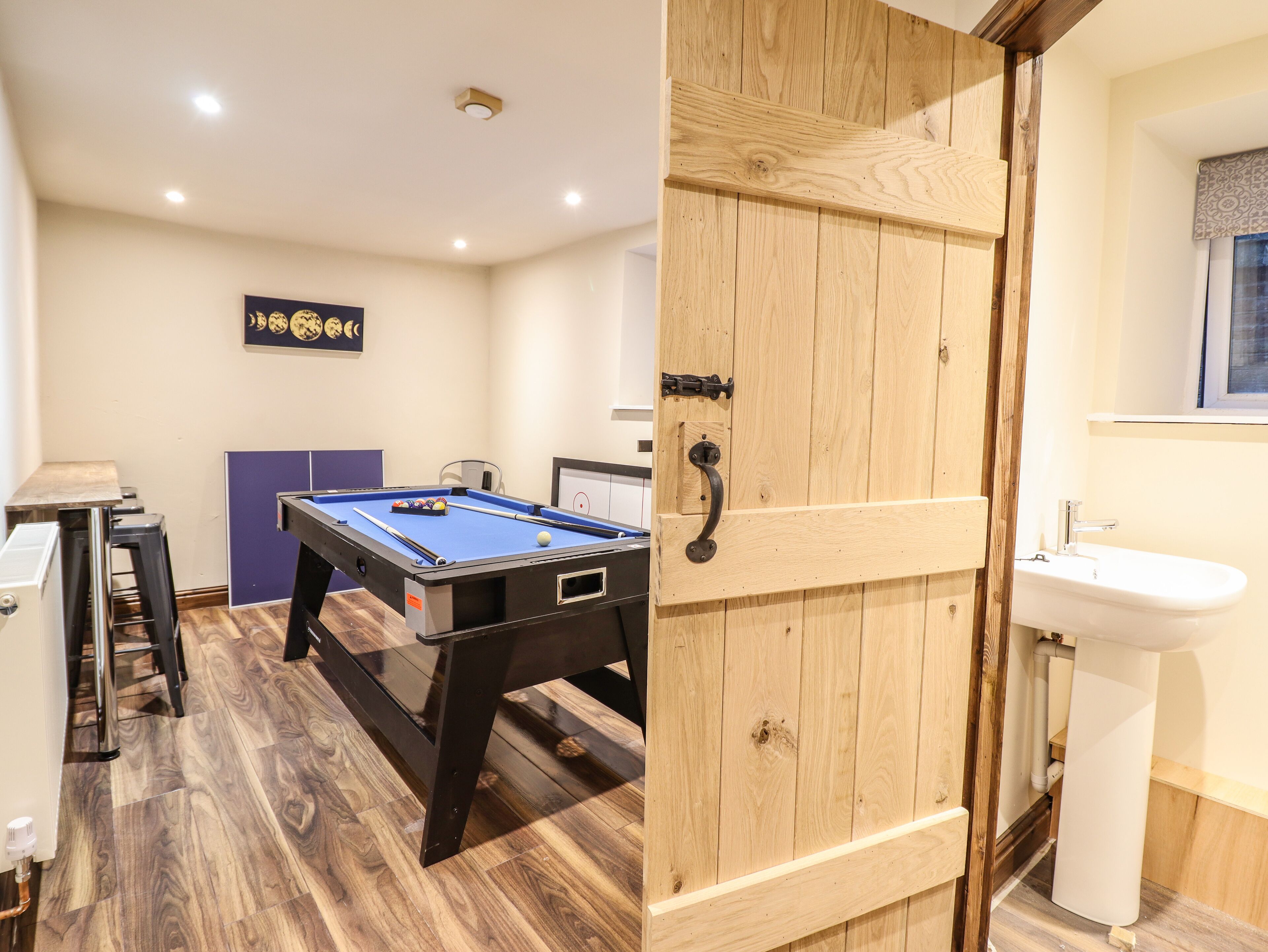 A room with a pool table, a wooden door, a sink, and a window with a patterned curtain.