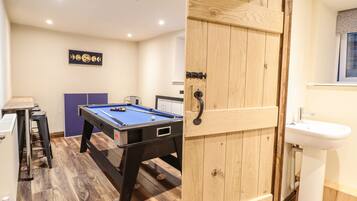 A room with a pool table, a wooden door, a sink, and a window with a patterned curtain.