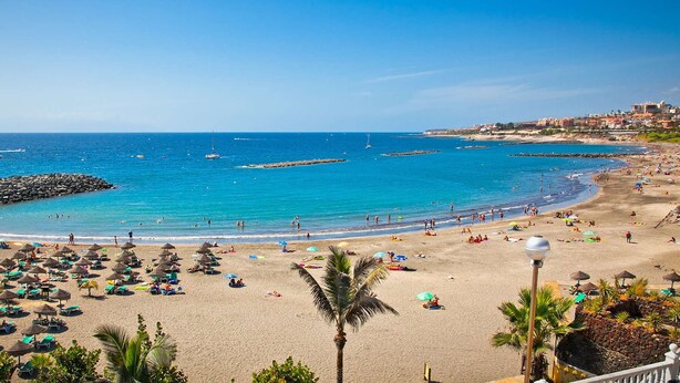 A beach with clear blue water, umbrellas, and people. - Tropical Green Park - Pool - Parking - La Corbeta Building (San Miguel de Abona)