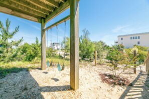 A covered outdoor area with swings, a wooden pergola, and a building in the background.