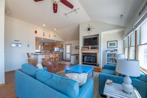 A spacious living room with a fireplace, a dining area, and a kitchen in the background.