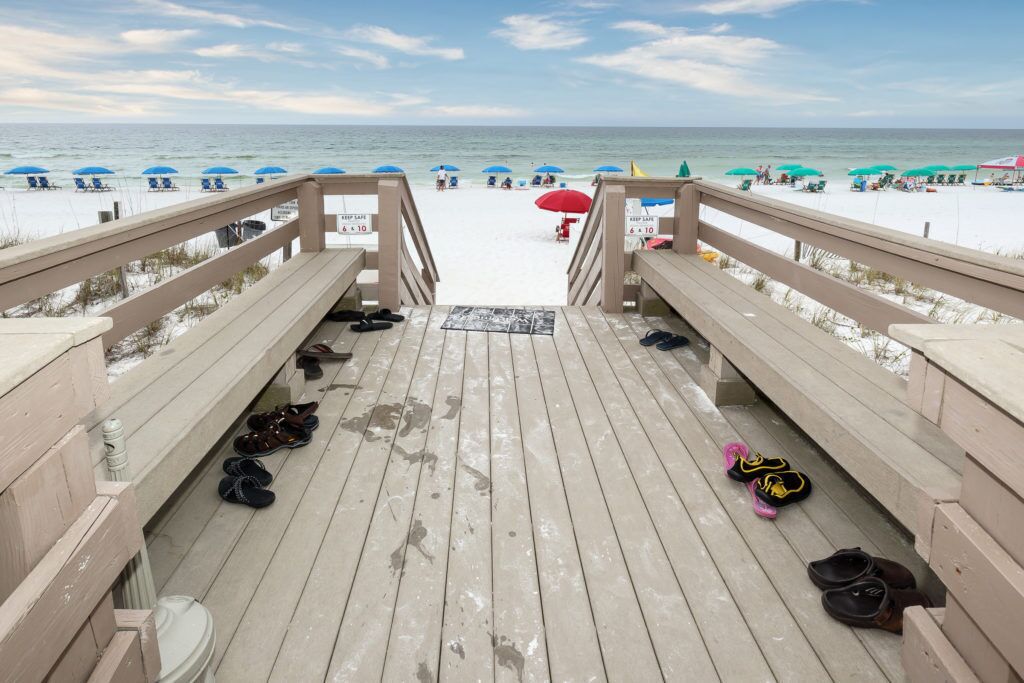 Een houten terras dat naar een strand leidt, met parasols en strandstoelen.