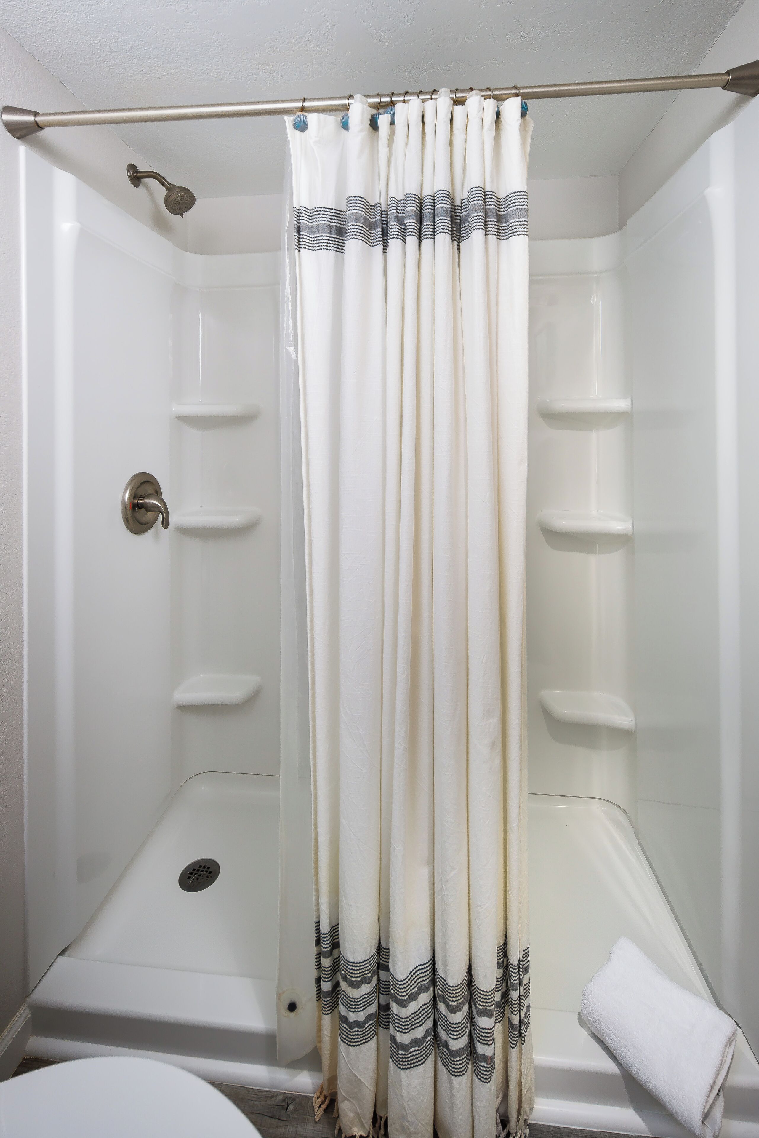 Une douche avec un rideau blanc et une tringle de douche en métal.