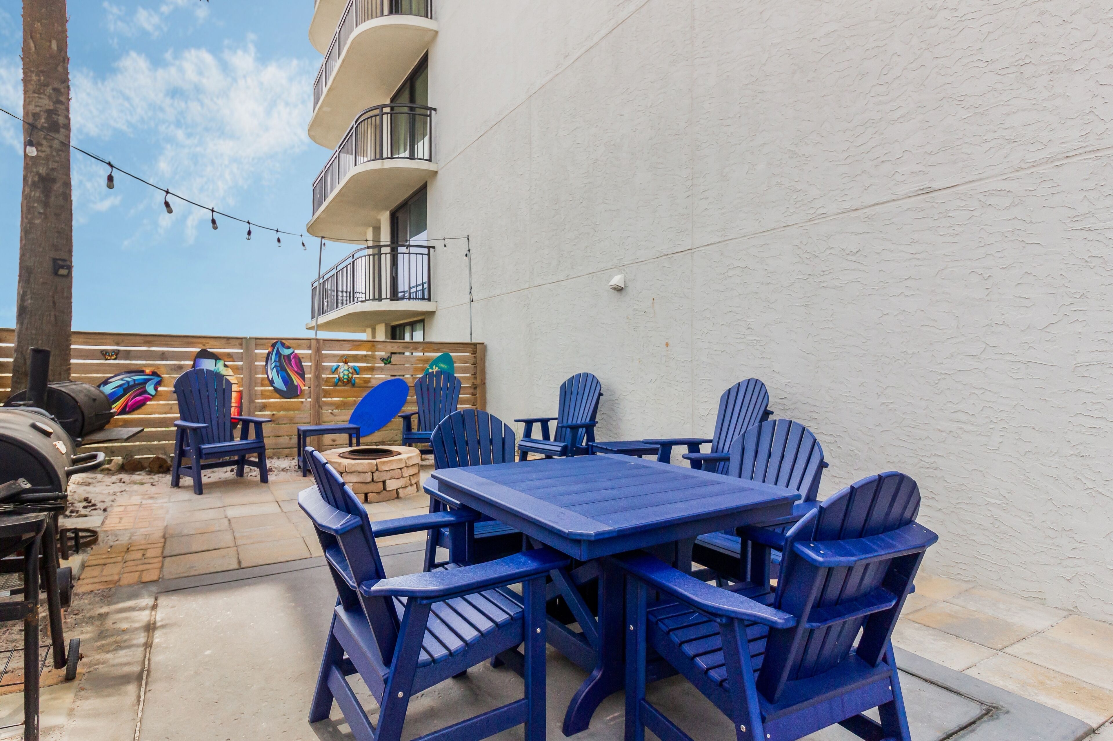 Un patio con sillas Adirondack azules, una mesa de madera y una parrilla.