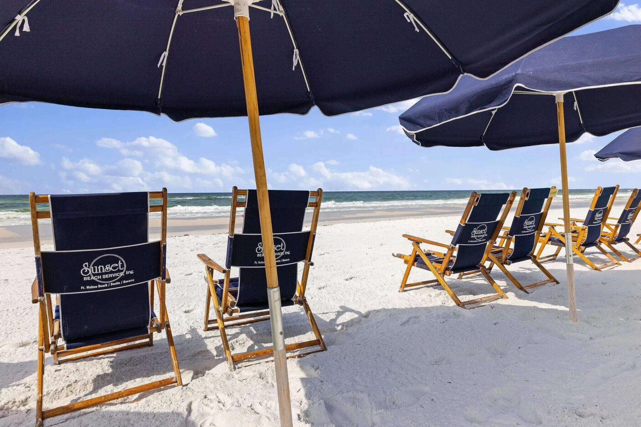 Sillas de playa con sombrillas en una playa arenosa.
