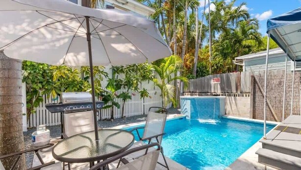 Un patio trasero con piscina, parrilla y un área de patio techada.
