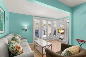 A living room with a sofa, armchair, and a television. - Poolside Paradise - Heated Pool & Steps to Duval St (Key West)