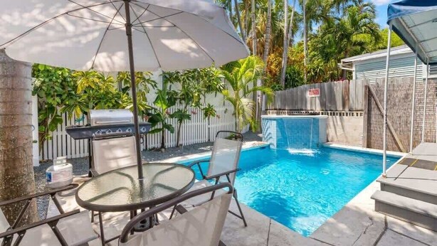 En baghave med swimmingpool, grill og et spiseområde med stole og en parasol.