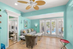 A living room with a sofa, armchair, and coffee table, a ceiling fan, and a view through glass doors to an outdoor area.
