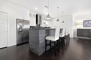 Una cocina moderna con armarios blancos, un refrigerador de acero inoxidable, una isla central con salpicadero negro e iluminación colgante.