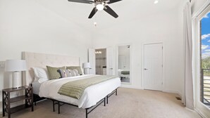 Un dormitorio con cama, mesitas de noche, ventilador de techo y un ventanal amplio.