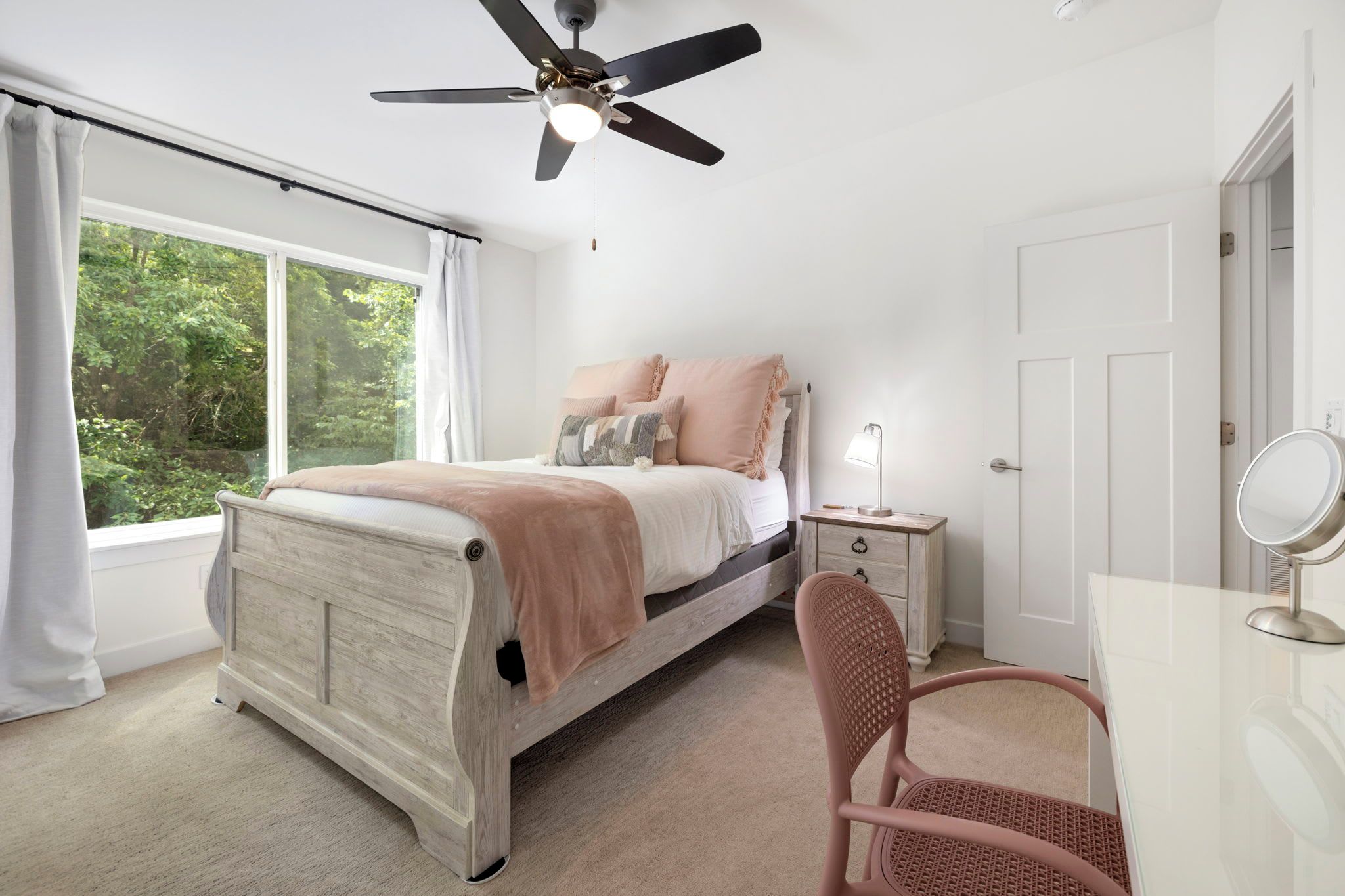 A bedroom with a bed, a desk, a chair, a ceiling fan, and a window with curtains.