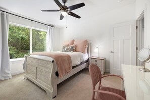 Un dormitorio con cama, escritorio, silla, ventilador de techo y ventana con cortinas.