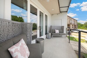 A balcony with a grey sofa, a patterned cushion, and a wicker partition. - Hilltop Haven - 5 Min to DT & UofA - Modern (Fayetteville)