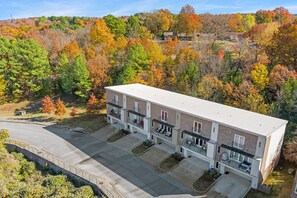 A multi-story building with a flat roof, a parking lot, and a backdrop of autumn-colored trees.