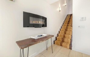 A staircase with a patterned carpet, a wooden bench, and a wall-mounted fireplace.