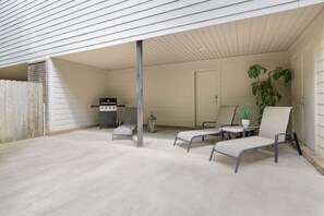 A covered outdoor patio with a concrete floor, a grill, a chair, a small table, and a potted plant.