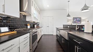 A modern kitchen with stainless steel appliances, black and white cabinetry, and a dark wood floor.