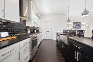 A modern kitchen with stainless steel appliances, black and white cabinetry, and a dark wood floor. - Hilltop Haven - 5 Min to DT & UofA - Modern (Fayetteville)