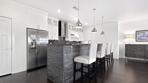 Una cocina moderna con armarios blancos, un refrigerador de acero inoxidable, una isla central con salpicadero negro e iluminación colgante.