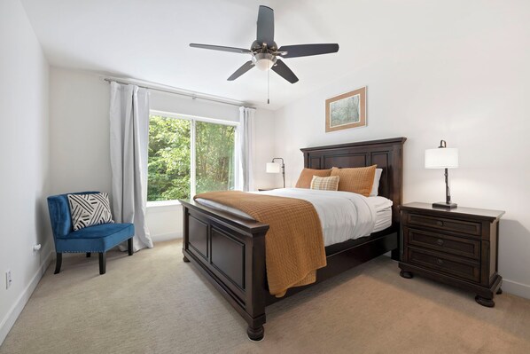 A bedroom with a bed, a nightstand, a chair, a ceiling fan, and a window with curtains.