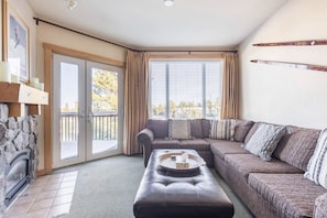 A cozy living room with a sectional sofa, a fireplace, and a large window with curtains.