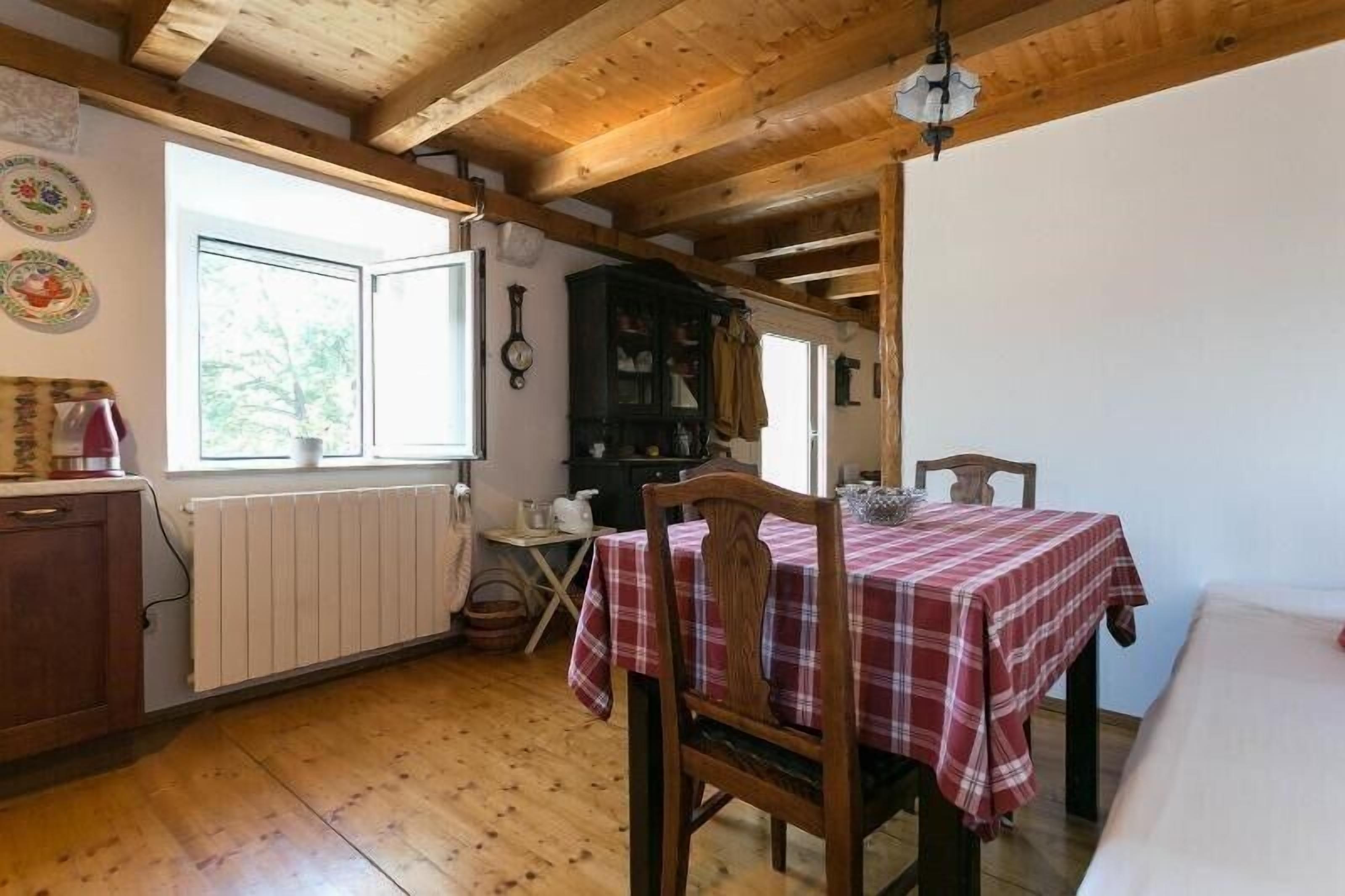 Un interior de fusta amb una taula de dinar coberta amb un mantell a cuadros, un radiador i una finestra que ofereix vistes a la vegetació.