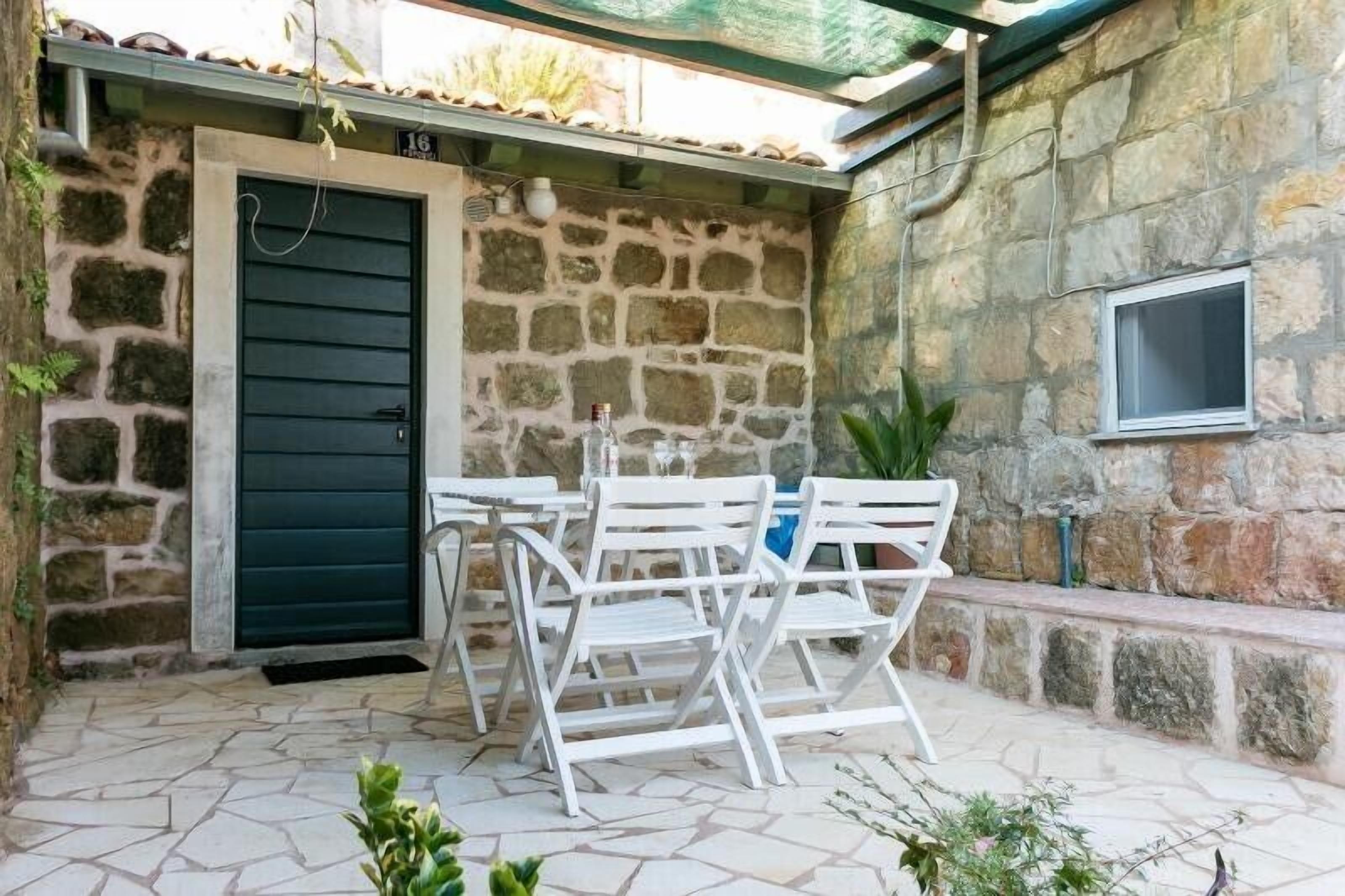 A stone-walled outdoor patio with a table and chairs, a door, and a window.