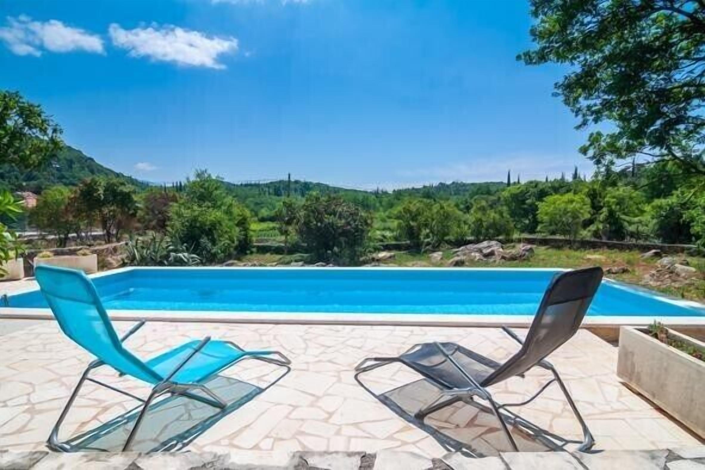 A swimming pool with two lounge chairs, surrounded by a stone patio and lush greenery.