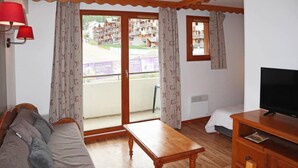 A room with a wooden sofa, a wooden table, a TV on a wooden stand, and a balcony with curtains. - Ski-in/ski-out & foot of the slopes, 1st floor, view ski slopes, swimming pool, sauna, balcony, tv (Les Orres)