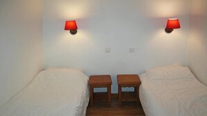 A room with two single beds, each with a wooden nightstand and a red wall lamp. - Ski-in/ski-out & foot of the slopes, 1st floor, view ski slopes, swimming pool, sauna, balcony, tv (Les Orres)