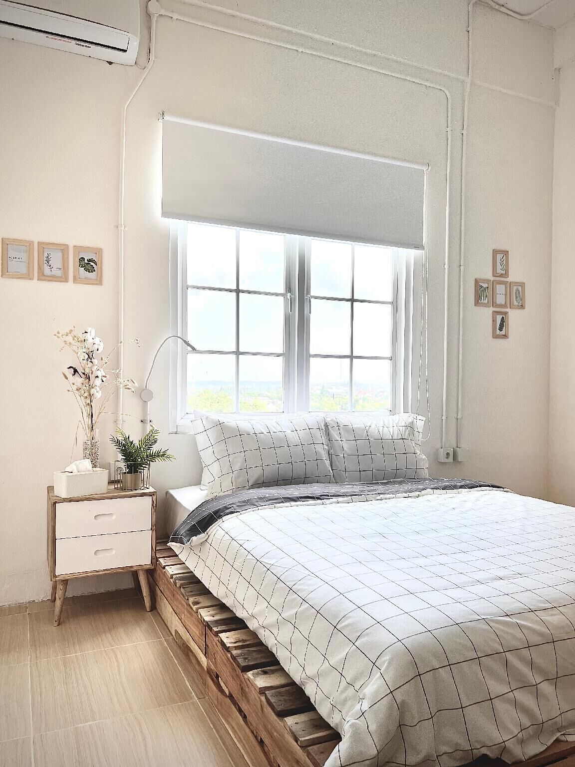 Un dormitorio con un ventanal grande, una mesita de noche con cajones, una lámpara de noche y una cama con colcha estampada.
